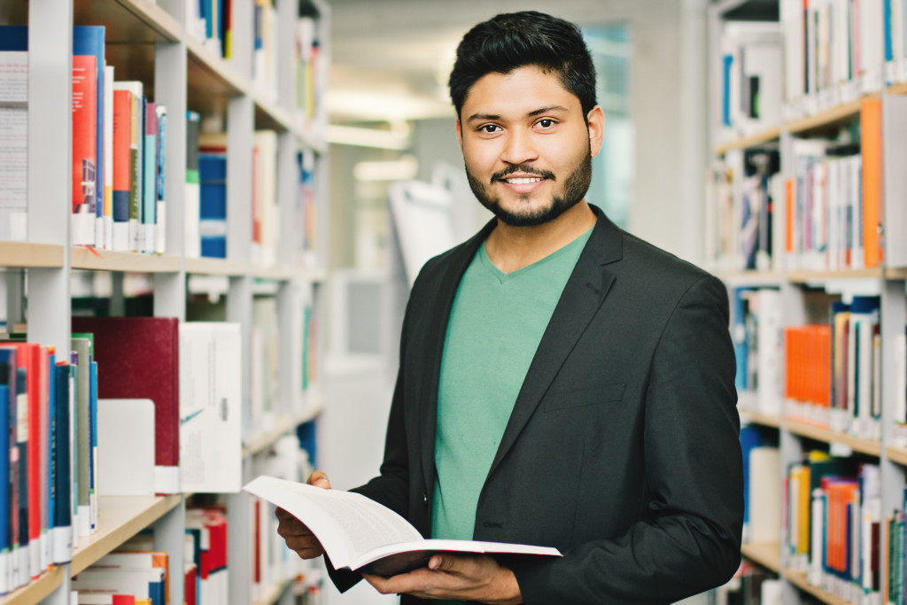 Young student smiling while holding an open book in a library.